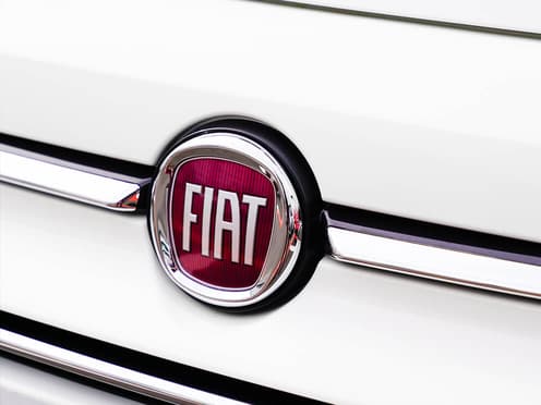 Gros plan sur le blason Fiat située à l'avant d'une voiture blanche de la marque italienne.