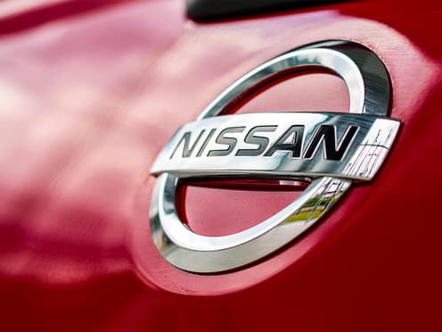 Gros plan sur le logo de la marque japonaise Nissan à l'avant d'une voiture rouge reprise par Aramisauto.