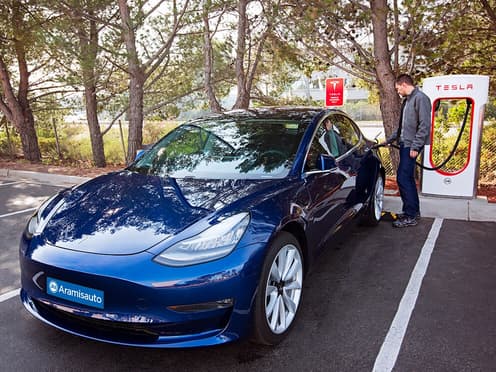 Un homme recharge sa Tesla bleue devant une borne de recharge Supercharger.