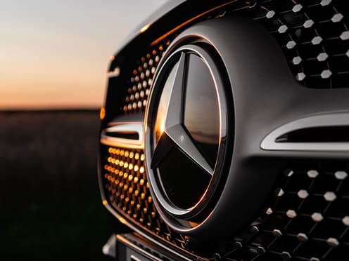 Gros plan sur le blason Mercedes à l'avant d'une voiture reprise par Aramisauto. La lumière se reflète sur le logo de la marque allemande.