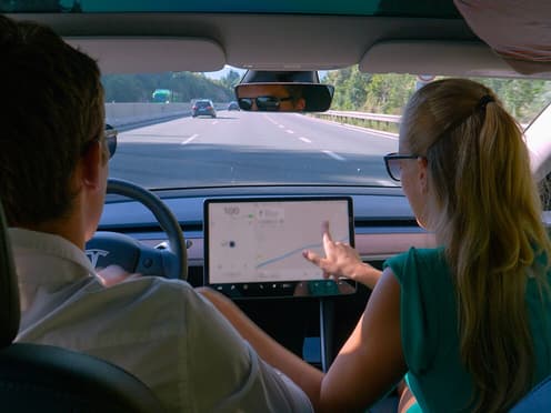 Un couple voyage dans une Tesla, la femme regarde le plan de la route sur l'écran tactile de la voiture.