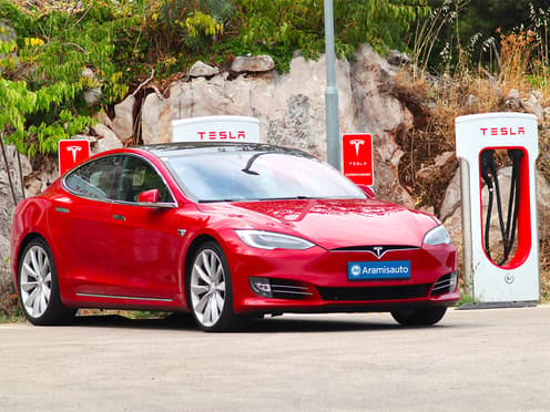 Une Tesla rouge est garée devant des bornes de recharge Supercharger.