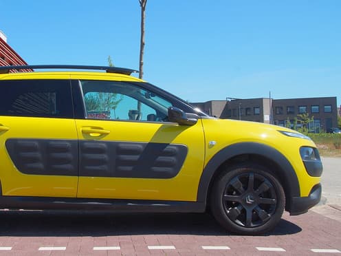 Une Citroën C4 Cactus jaune reprise par Aramisauto est garée en ville au bord d'une route.