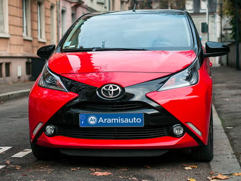 Une Toyota Aygo rouge reprise par Aramisauto est garée en ville.