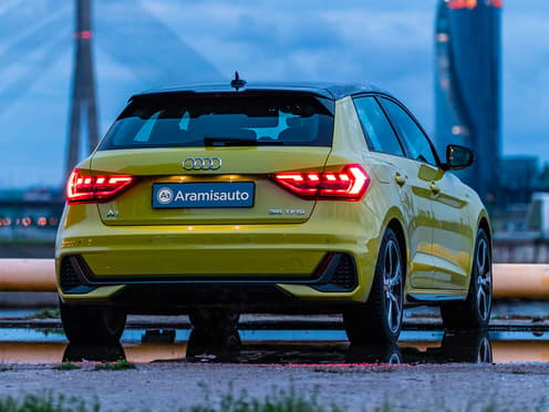 Une Audi A1 Sportback jaune reprise par Aramisauto roule sur un port à la tombée de la nuit.