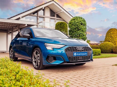 Une Audi A3 Sportback bleue reprise par Aramisauto est garée dans l'allée de garage d'une maison.