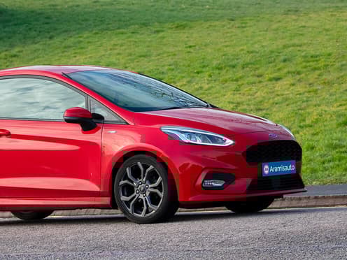 Une Ford Fiesta rouge reprise par Aramisauto roule sur une route.